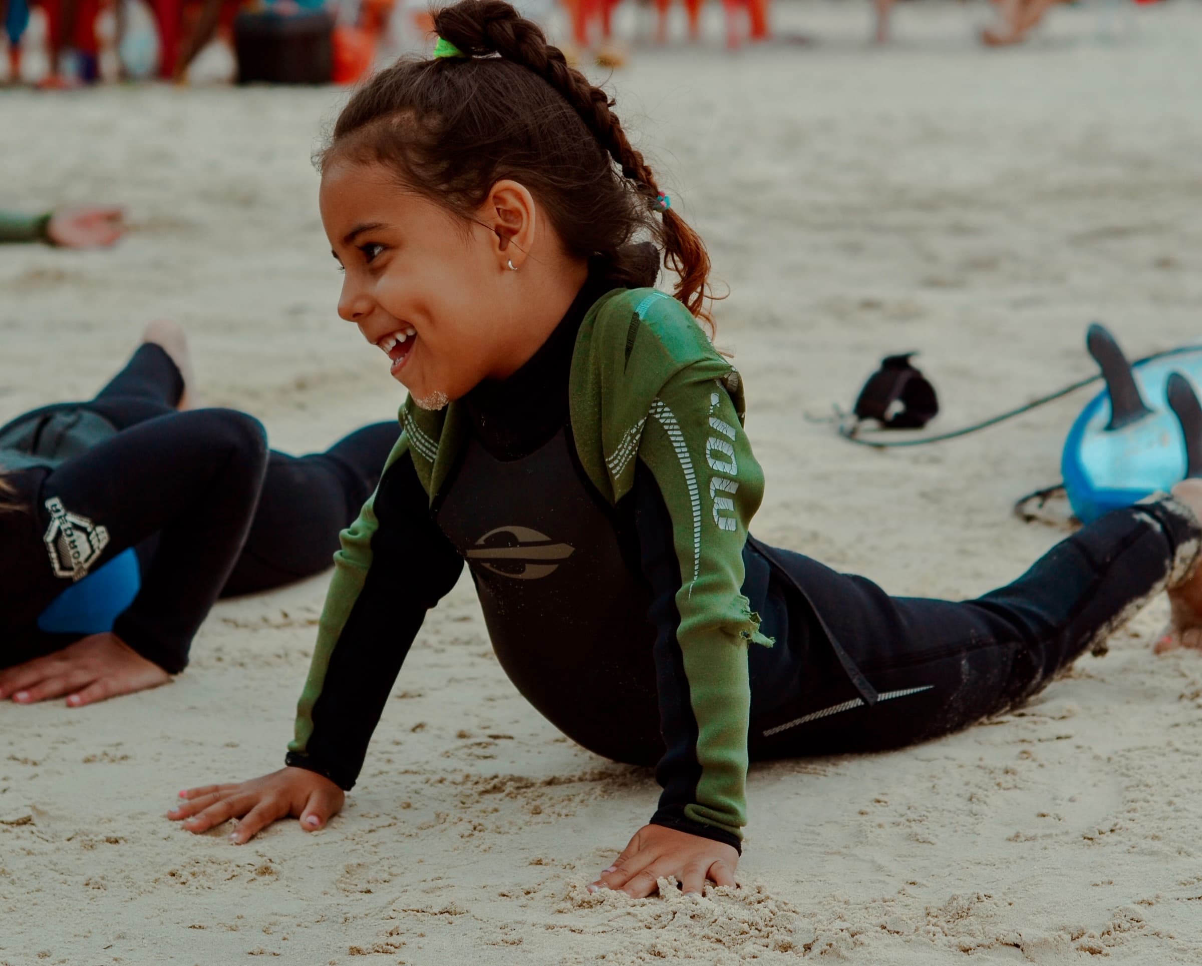 Uma menina sorridente de neoprene se apoiando com os braços na areia.