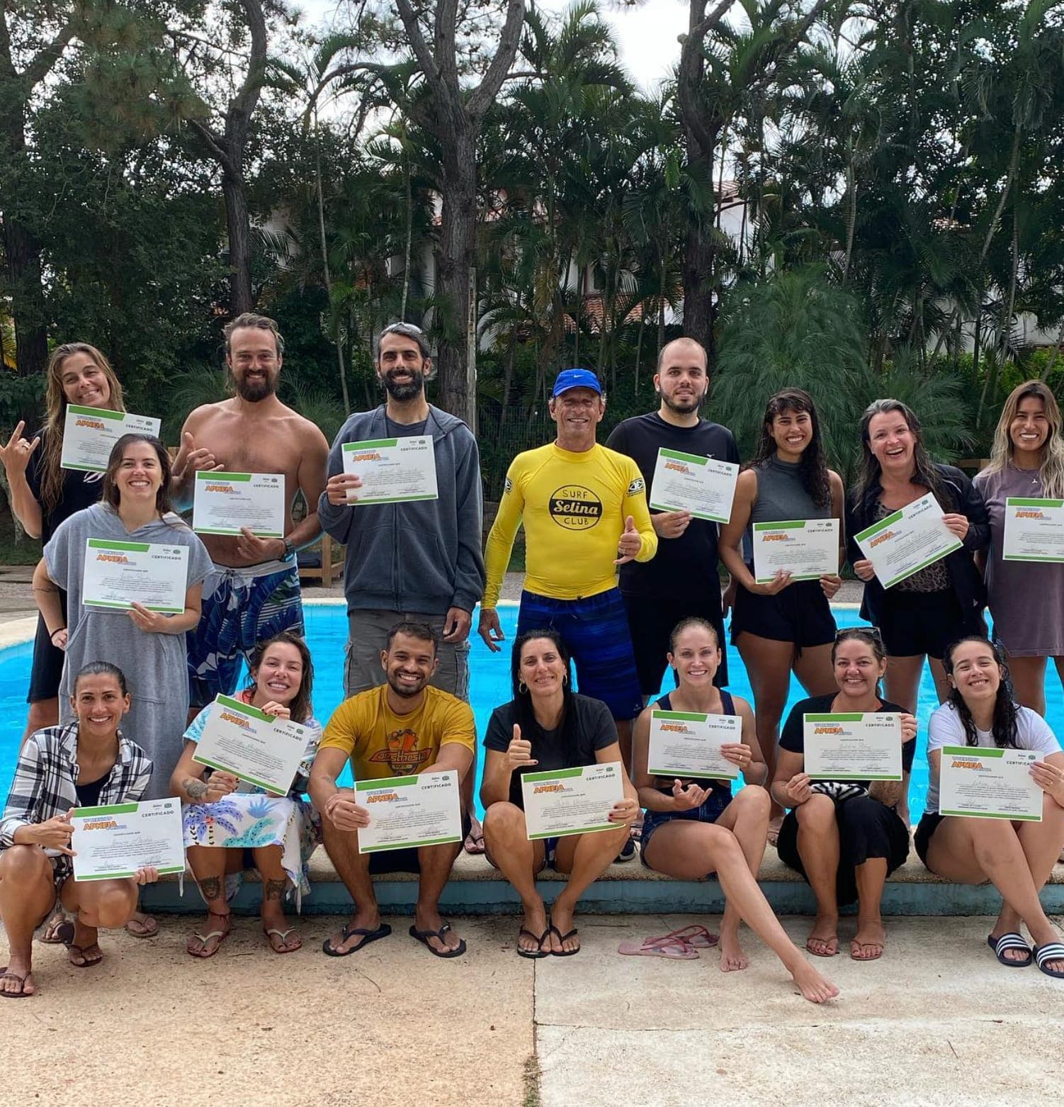 Grupo de alunos segurando seus certificados ao redor de uma piscina.
