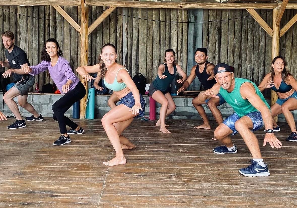 Grupo fazendo agachamentos juntos em um deck de madeira.