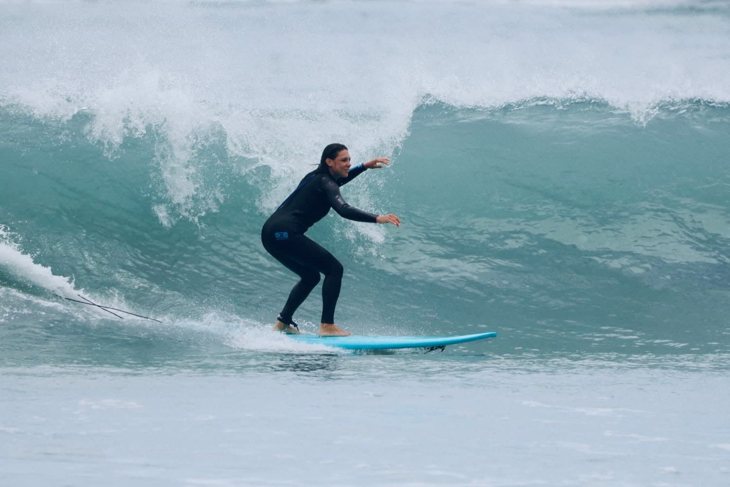 A surfer in a black wetsuit riding down a wave on a blue board in Barra da Lagoa.
