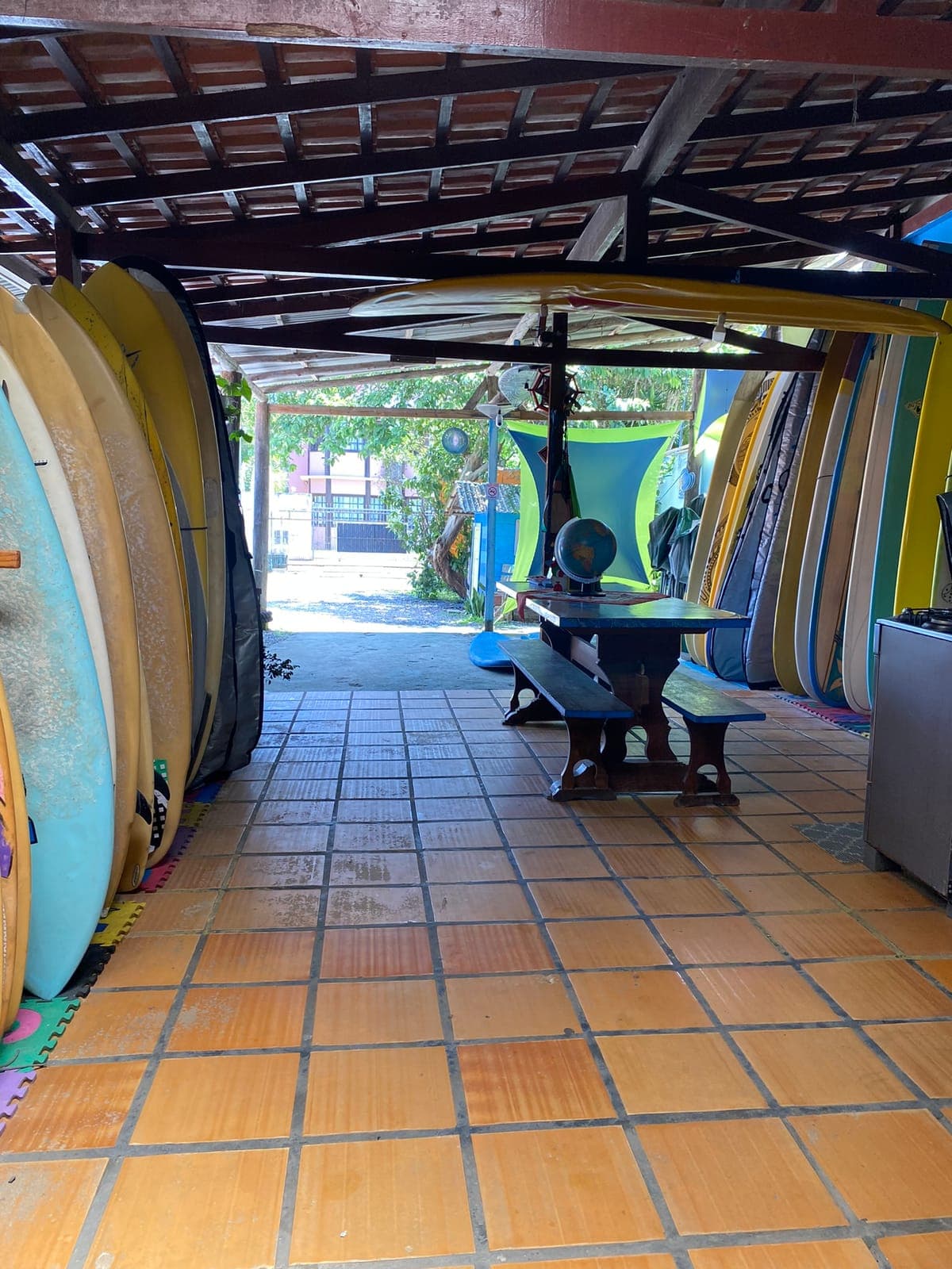 A covered patio with surfboards stacked along the walls and a wooden picnic table under the roof.