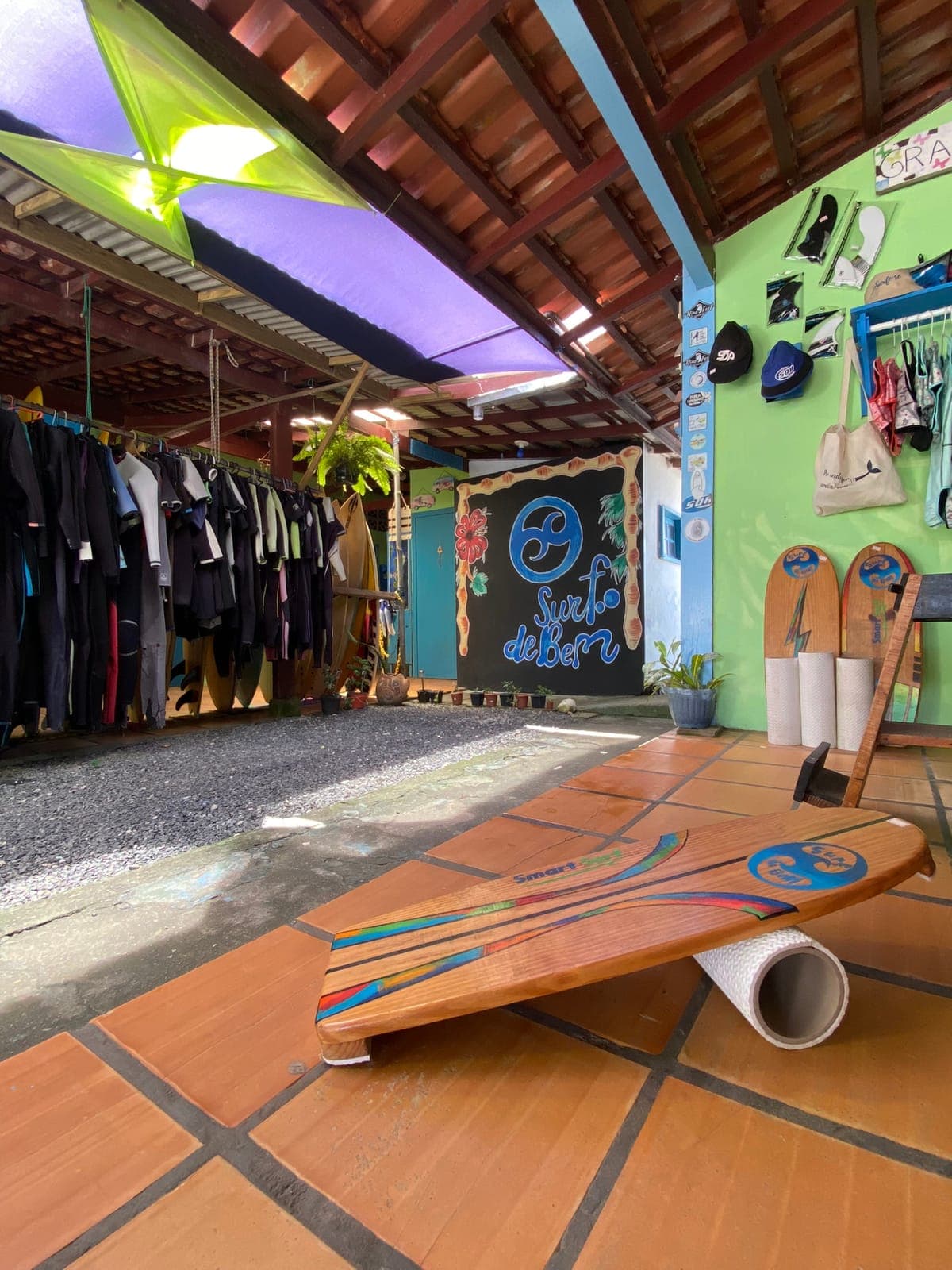 Wetsuits hanging on a rack next to a balance board, under a colorful roof.