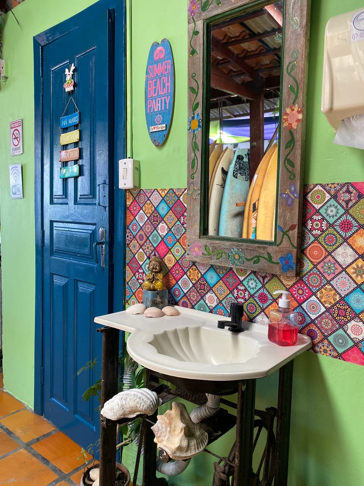 A blue door beside a hand-painted sink and a mirror framed with mosaic tiles.