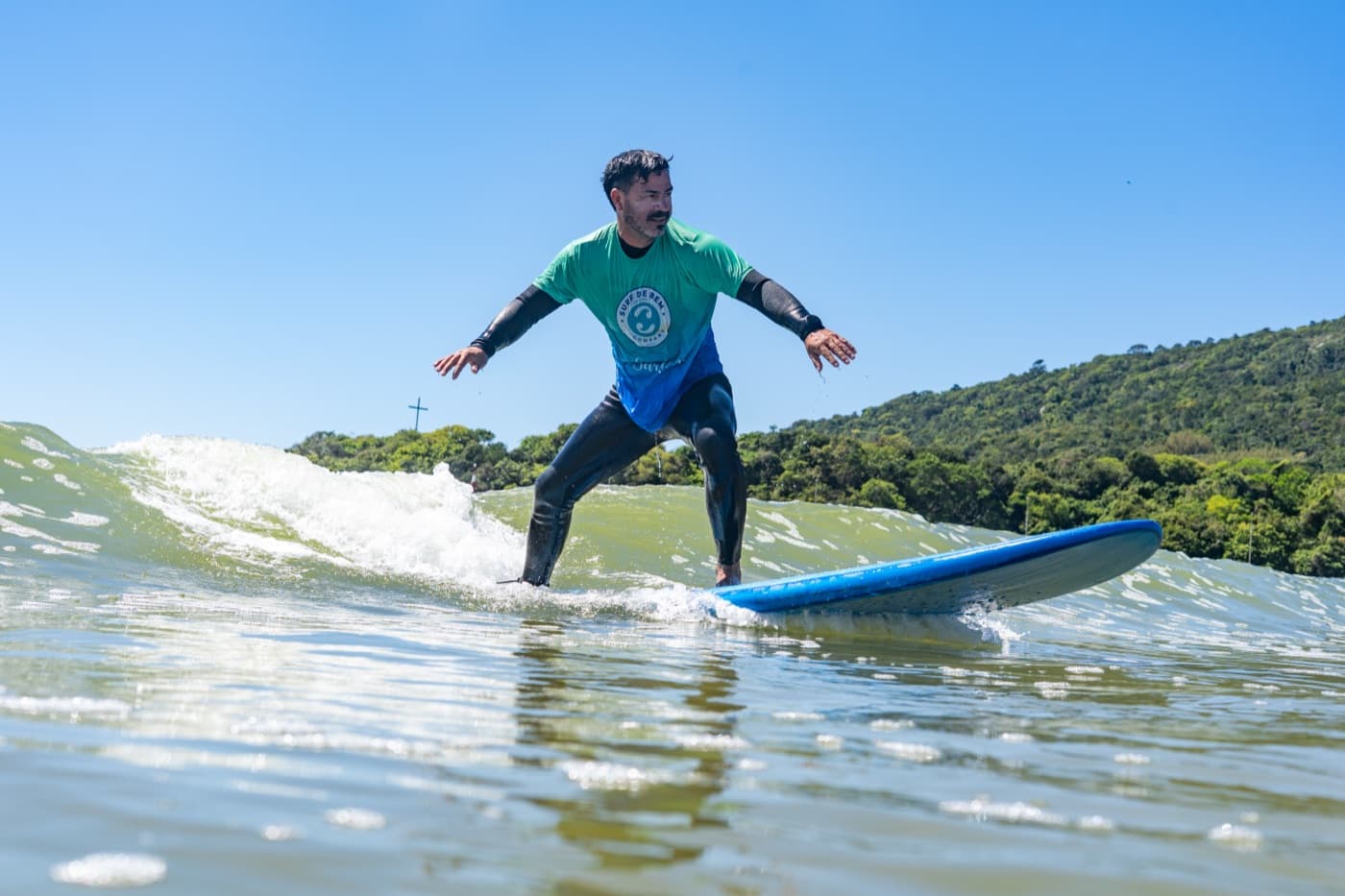 Um surfista em uma pequena onda, em uma prancha azul.