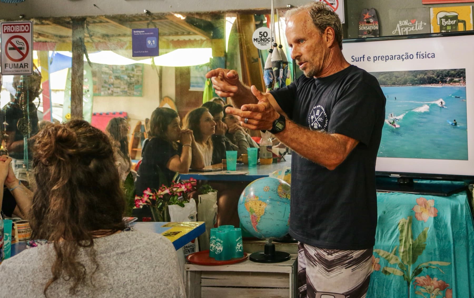 A coach explaining surf and physical preparation to a class, with a wave on the screen behind him.