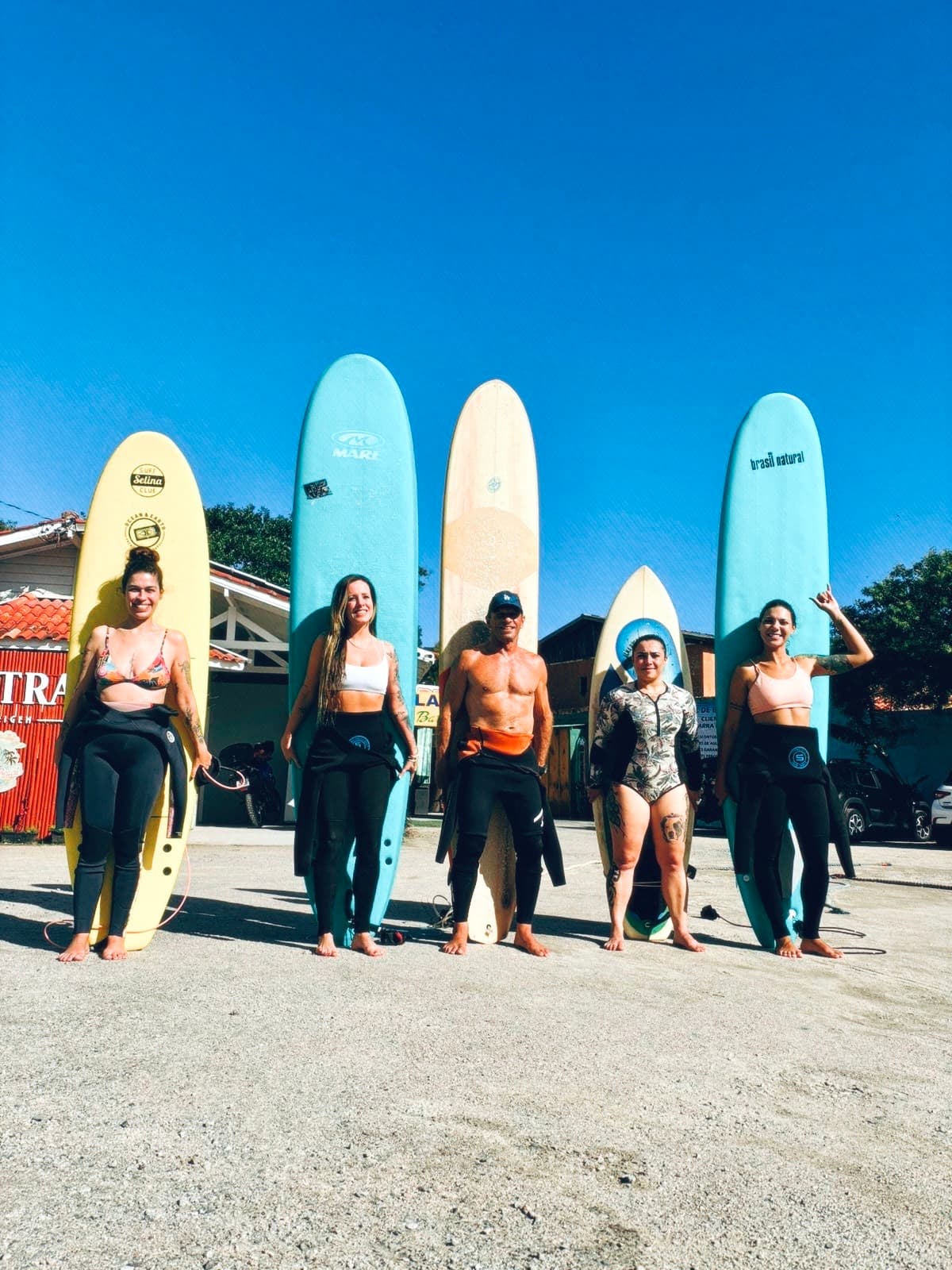Students and a coach standing in front of their tall surfboards on a sunny day.