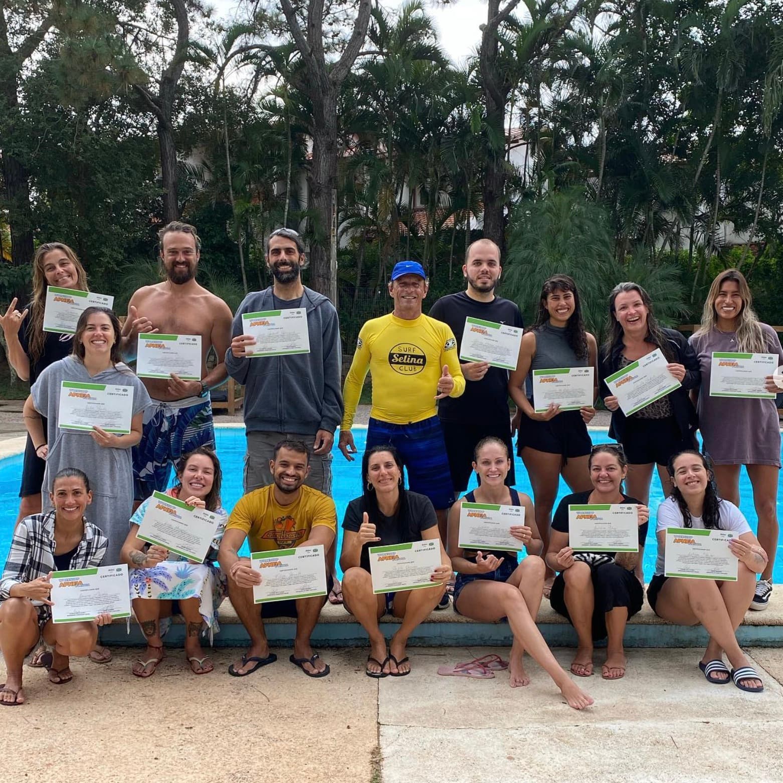 A group of students holding their course certificates beside a pool.