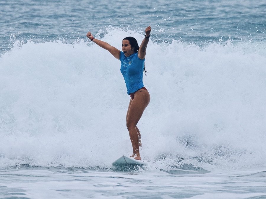 Surfista de camisa azul surfando uma onda com os dois braços erguidos
